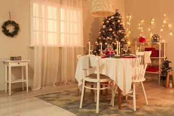 Festive table setting with burning candles and Christmas decorations in dining room at evening