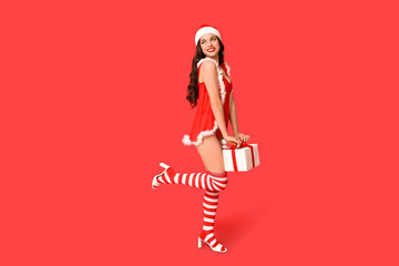 Beautiful young sexy woman in Santa hat with Christmas gift box on red background