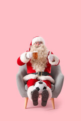 Santa Claus with mug of beer and soccer ball in armchair on pink background
