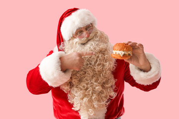 Santa Claus pointing at tasty burger on pink background