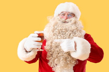 Santa Claus pointing at glass of beer on yellow background