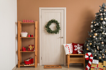 Interior of festive room with Christmas tree, gift boxes, glowing lights and wreath on door