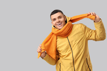 Young man in yellow stylish jacket and scarf on grey background