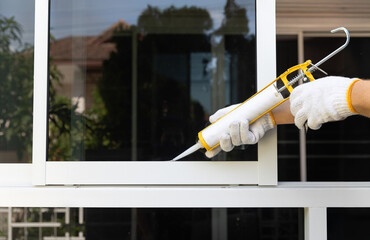 Construction worker using silicone sealant caulk for repair leaked inside window frame.