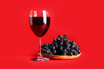 Glass of wine with grapes on red background