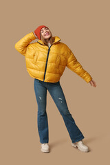 Fototapeta premium Beautiful young happy woman in warm winter clothes on brown background