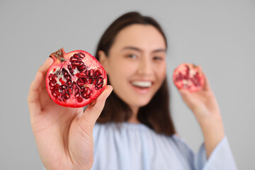 Beautiful young woman with fresh pomegranate on grey background