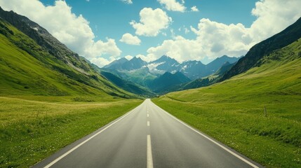 Fototapeta premium A long, straight road stretches through a lush green valley, leading towards majestic snow-capped mountains in the distance under a bright blue sky.