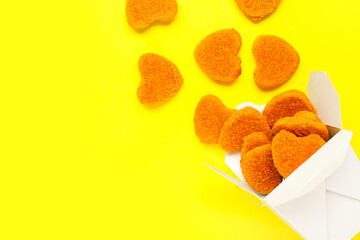 Paper box with tasty nuggets in shape of heart on yellow background. Valentine's Day celebration