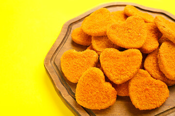 Wooden board with tasty nuggets in shape of heart on yellow background. Valentine's Day celebration