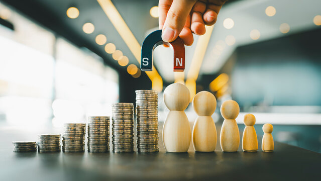 Business executive holding a magnet to attract a pile of money and a model of a group of people is a concept about earning income, growing the company along with finding the right people to work with.