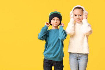 Cute little happy children in warm winter clothes on yellow background