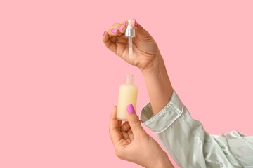 Female hands with bottle of cosmetic serum on pink background