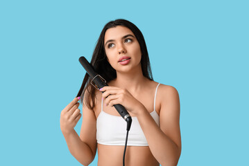 Beautiful young woman with curling iron  against color background