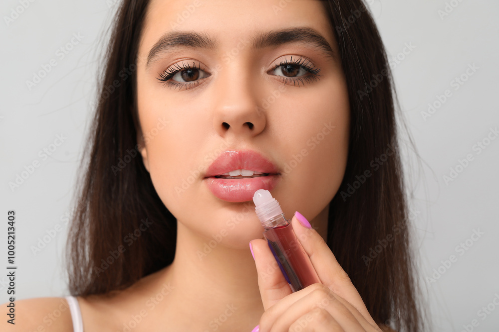 Poster Beautiful young woman with lipgloss on grey background, closeup