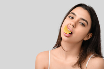 Beautiful young woman with half of lemon in her mouth on grey background