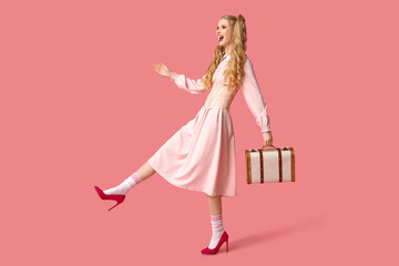 Beautiful young happy woman dressed as doll with suitcase on pink background