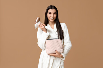 Beautiful young happy woman in bathrobe with modern photoepilator and cosmetic bag on brown background