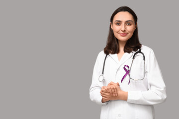Young female doctor with purple ribbon on grey background. Pancreatic cancer awareness concept