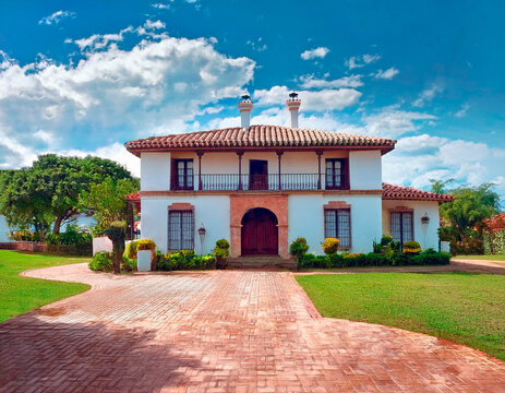 Casa modelo campestre de dos pisos con teja espa&ntilde;ola, camino en ladrillado de color marr&oacute;n.
