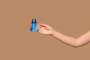 Female hand with blue ribbon on beige background. Colon cancer awareness concept