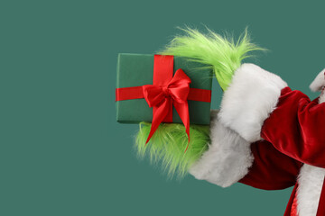 Hairy hands of creature in Santa costume with Christmas gift box on green background