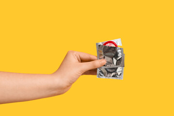 Female hand with condoms on yellow background, closeup