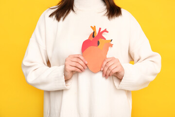 Woman holding paper human heart on yellow background, closeup