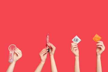 Female hands with condoms and vibrator on red background