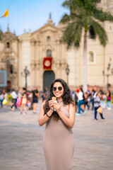 Fototapeta premium Young Latina woman smiling and enjoying a snack at Plaza Mayor in Lima, Peru, surrounded by historical architecture.