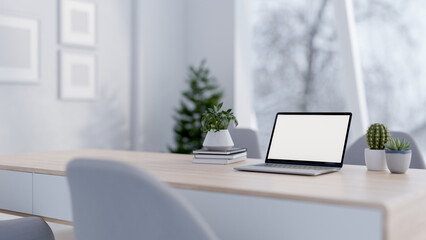 A close-up of a laptop with a white screen mockup placed on a minimalist desk in a white room.