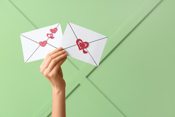 Female hands holding paper envelopes with hearts on green background. Valentine's Day celebration