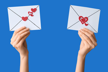 Female hands holding paper envelopes with hearts on blue background. Valentine's Day celebration