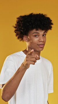 Vertical video. Heart gesture. Love sign. Confident guy flirting blowing air kiss expressing adore romantic affection isolated on yellow background.