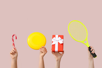 Female hands holding candy cane, frisbee, gift and tennis racket on pink background. Christmas...