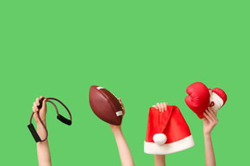 Female hands holding expander, rugby ball, boxing gloves and Santa hat on green background. Christmas sport composition