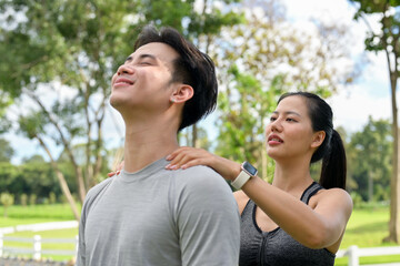 Obraz premium A woman is massaging her boyfriend's shoulders after jogging together in a public park.