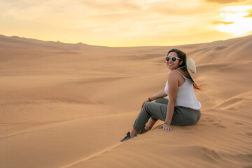 Young woman sitting and relaxing on the sand dunes in Huacachina, Ica, Peru, during a stunning sunset, enjoying the tranquil desert.