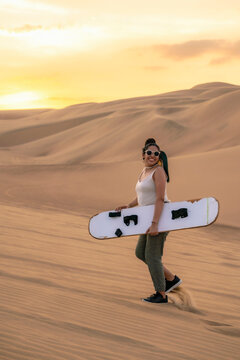 Young woman holding her sandboard high in excitement after a fun ride down the sand dunes in Huacachina, Ica, Peru.