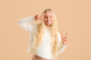 Happy teenager girl showing victory gesture on beige background