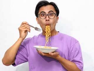 Young Asian man eating fried noodles with a funny shocked expression, isolated on a white...