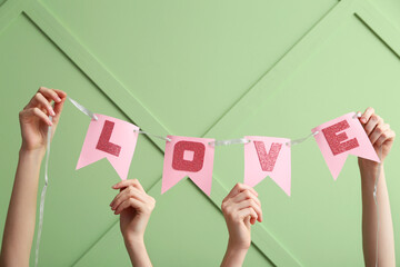 Obraz premium Women holding paper flags with word LOVE against color wall, closeup. Valentine's Day celebration