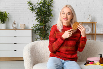 Mature woman brushing hair while sitting on sofa at home