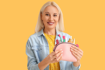 Beautiful mature woman holding bag with cosmetics and makeup accessories on color background