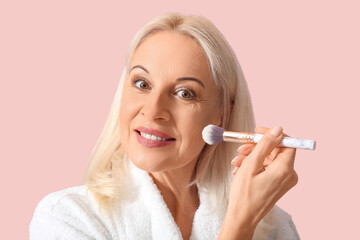 Beautiful mature woman with makeup brush on color background, closeup