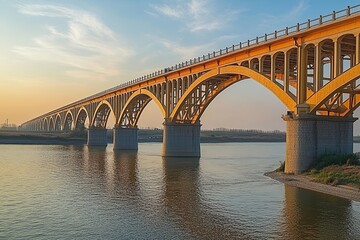 Fototapeta premium A large yellow bridge spans a river at sunset.