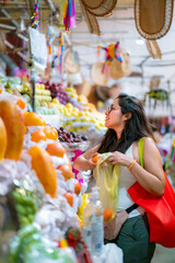 Young Latina woman smiling while shopping for fresh produce at a colorful market stall in Mexico City, Mexico.