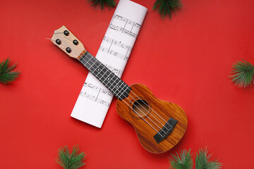 Composition with ukulele, music sheet and fir branches on red background
