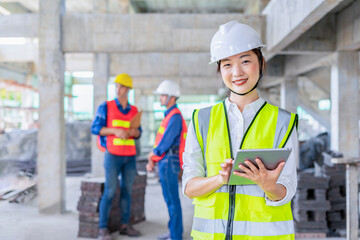 asian female engineer holds digital tablet,smiling and posing to camera,background the colleagues team inspecting under construction building