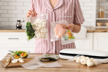 Young woman with vacuum sealer machine, meat and vegetables in packs on kitchen table